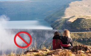 Two girls on hill sitting across hydrodam